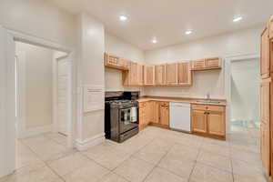 Kitchen featuring white dishwasher, light tile patterned flooring, light brown cabinetry, and black range with gas cooktop