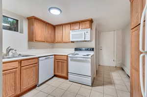 Kitchen featuring a baseboard radiator, white appliances, light tile patterned flooring, and sink