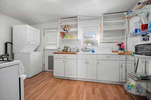 Kitchen featuring light hardwood / wood-style flooring, stacked washer / dryer, white cabinetry, and garden window