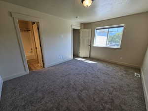 Unfurnished bedroom featuring a closet, a textured ceiling, carpet flooring, ensuite bath, and a walk in closet