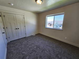 Unfurnished bedroom featuring dark carpet, a mountain view, a closet, and a textured ceiling