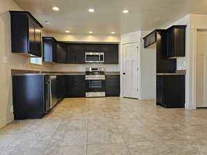 Kitchen with dark stone countertops, a textured ceiling, and appliances with stainless steel finishes