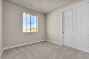 Unfurnished bedroom featuring a closet, a textured ceiling, and light colored carpet