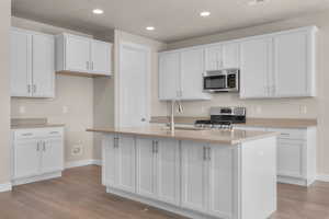 Kitchen with appliances with stainless steel finishes, white cabinets, a kitchen island with sink, and light wood-type flooring