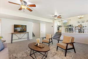 Living room featuring ceiling fan with notable chandelier and light carpet