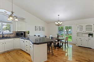 Kitchen with a kitchen breakfast bar, white cabinets, kitchen peninsula, decorative light fixtures, and a notable chandelier