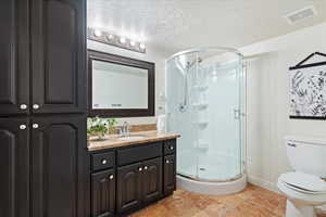 Bathroom featuring a textured ceiling, vanity, toilet, and an enclosed shower