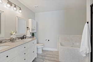 Bathroom featuring wood-type flooring, tiled bath, vanity, and toilet