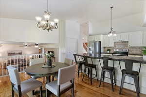 Dining room featuring ceiling fan with notable chandelier, high vaulted ceiling, and light hardwood / wood-style flooring