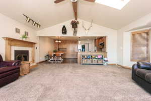 Living room featuring rail lighting, a tiled fireplace, carpet flooring, ceiling fan, and vaulted ceiling with beams