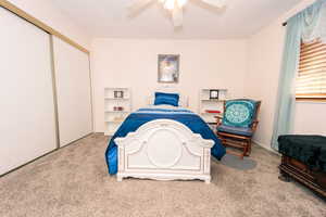 Carpeted bedroom with ceiling fan and a closet