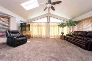 Living room with carpet, lofted ceiling with skylight, and ceiling fan