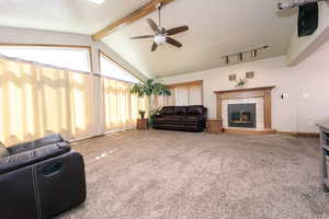 Living room featuring ceiling fan, vaulted ceiling with beams, carpet floors, and a tiled fireplace