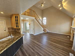 Kitchen with new dark wood-type flooring, a textured ceiling, dark stone countertops, lofted ceiling, and ceiling fan