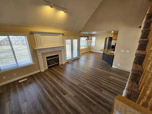 Unfurnished living room with a tiled fireplace, a notable chandelier, new dark wood-type flooring, high vaulted ceiling, and sink