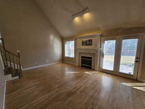 Unfurnished living room featuring wood-type flooring, lofted ceiling, a tiled fireplace, and track lighting