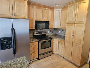 Kitchen featuring dark stone countertops, backsplash, light brown cabinets, stainless steel appliances, and light wood-type flooring