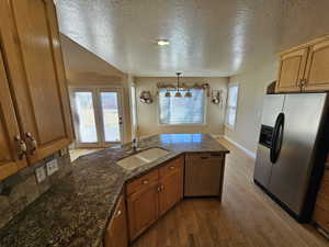 Kitchen featuring hanging light fixtures, sink, dark stone counters, appliances with stainless steel finishes, and light wood-type flooring