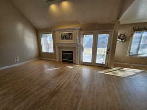 Unfurnished living room with wood-type flooring, a textured ceiling, a tiled fireplace, and vaulted ceiling