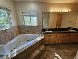 Bathroom with a healthy amount of sunlight, a textured ceiling, a relaxing tiled tub, and vanity