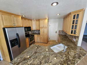 Kitchen with appliances with stainless steel finishes, tasteful backsplash, kitchen peninsula, light hardwood / wood-style flooring, and dark stone counters