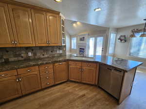 Kitchen with dishwasher, light hardwood / wood-style floors, sink, lofted ceiling, and kitchen peninsula