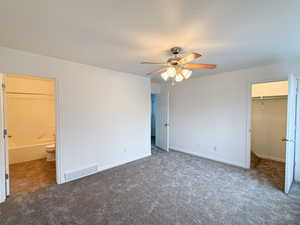 Unfurnished bedroom with dark carpet, ensuite bath, ceiling fan, a spacious closet, and a closet