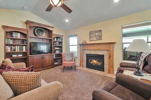 Living room featuring ceiling fan, light colored carpet, a tiled fireplace, and vaulted ceiling