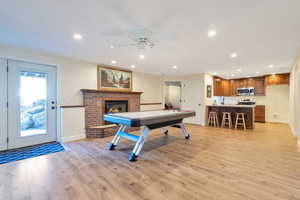 Rec room with light hardwood / wood-style flooring, a brick fireplace, and ceiling fan