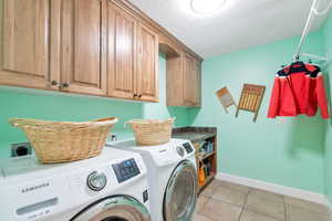 Laundry area with cabinets, a textured ceiling, light tile patterned floors, and washing machine and dryer