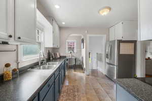 Kitchen with stainless steel refrigerator with ice dispenser, gray/blue bottom cabinets paired with white uppers, and a stainless steel  sink.