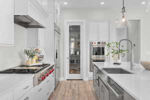 Kitchen with light hardwood / wood-style flooring, appliances with stainless steel finishes, decorative light fixtures, and white cabinetry