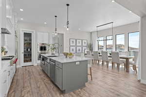 Kitchen featuring hanging light fixtures, light hardwood / wood-style floors, gray cabinetry, white cabinets, and a kitchen island with sink