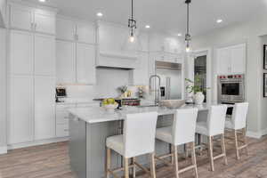 Kitchen featuring white cabinets, pendant lighting, a center island with sink, stainless steel appliances, and a kitchen bar