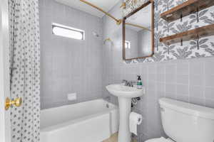 Bathroom featuring tile walls, toilet, and shower / bathtub combination with curtain