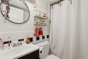 Bathroom with vanity, tile walls, toilet, and tasteful backsplash