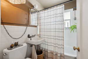 Bathroom with tile walls, shower / tub combo, toilet, and decorative backsplash