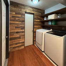 Laundry area with wood walls, washing machine and dryer, light hardwood / wood-style floors, and a textured ceiling