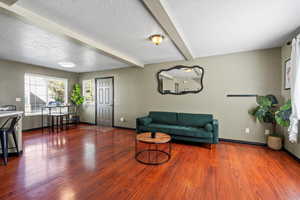 Living room with wood-type flooring, a textured ceiling, and beamed ceiling