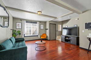 Living room with a textured ceiling, beamed ceiling, and dark wood-type flooring