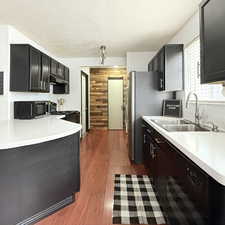 Kitchen featuring dishwasher, stove, sink, a textured ceiling, and wood-type flooring