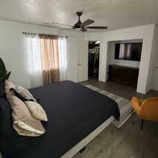 Bedroom with a textured ceiling, dark hardwood / wood-style flooring, a closet, and ceiling fan