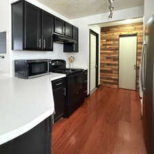 Kitchen with a textured ceiling, wood walls, dark wood-type flooring, and appliances with stainless steel finishes