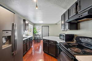 Kitchen with stainless steel appliances, a textured ceiling, and dark hardwood / wood-style floors