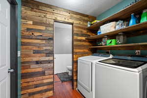 Washroom featuring washing machine and clothes dryer, wood walls, a textured ceiling, and dark hardwood / wood-style flooring