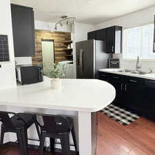 Kitchen with sink, dark wood-type flooring, a kitchen breakfast bar, stainless steel fridge with ice dispenser, and a textured ceiling