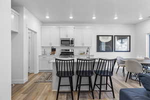 Kitchen with light hardwood / wood-style floors, a kitchen island with sink, white cabinetry, a kitchen breakfast bar, and appliances with stainless steel finishes *Photo is of an existing home of the same layout. Colors for listed home could vary*