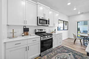 Kitchen with appliances with stainless steel finishes, decorative backsplash, light hardwood / wood-style flooring, and white cabinets *Photo is of an existing home of the same layout. Colors for listed home could vary*