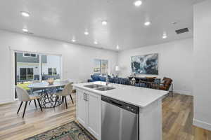 Kitchen with light wood-type flooring, sink, an island with sink, white cabinets, and stainless steel dishwasher *Photo is of an existing home of the same layout. Colors for listed home could vary*