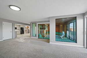 Unfurnished living room featuring a textured ceiling and light carpet